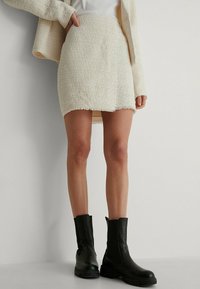 Mini-jupe blanche texturée avec un ourlet effiloché, portée avec des bottines noires à semelle épaisse et finition en cuir lisse.