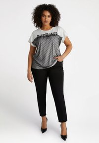 Svarta smala byxor i kombination med en grå och vit kortärmad topp. Toppen har en grafik med texten "DAYDREAMER" och ett prickigt mönster.