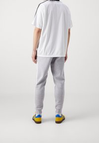 Vit kortärmad skjorta med svarta sidosträck, kombinerad med grå sweatpants som har vita sidosträck och gula skor med blå accenter.