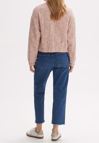 Różowy sweter szydełkowy z krojem skróconym, w zestawie z niebieskimi dżinsami z surowym wykończeniem. Dodatkiem są białe i beżowe trampki.