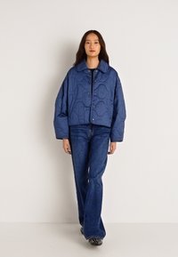 Κοντραρισμένο μπλε επενδυμένο μπουφάν με στρογγυλή κολάρο, κουμπιά με πατήματα και υφή σε κυματιστό σχεδιασμό, που συνδυάζεται με φαρδιά μπλε τζιν. 