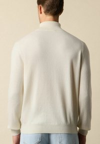 Sweter z dzianiny w kolorze kremowym, z wysokim kołnierzem, prążkowanymi mankietami i dołem, o miękkim, teksturowanym wykończeniu. Tylny widok ukazuje luźny krój.