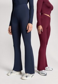 Leggings a zampa blu e bordeaux realizzati in un tessuto elastico. Entrambi presentano una vita alta e texture morbide, abbinati a scarpe sportive.