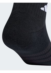 Schwarze Sportsocke mit strukturiertem Strickmuster, verstärktem Fersenbereich, glatter Zehenpartie und weißen Markenakzenten nahe der Bündchenkante.