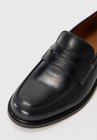 Black leather loafers with a rounded toe, visible stitching, and a decorative strap across the front. Smooth texture and classic design.
