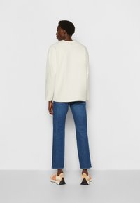 Lys beige langærmet bluse, blå straight-leg jeans og multicolore sneakers med en struktureret sål. Enkel design, minimale mønstre.