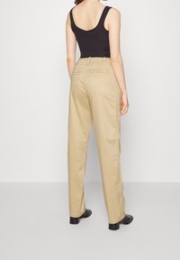Pantalon beige à jambes droites en coton. Dispose de deux poches arrière et de détails de couture subtils. Assorti à un débardeur noir et des bottes à talons.