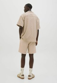 Cămașă bej cu model, cu mânecă scurtă, și pantaloni scurți asortati, ambele dintr-un material texturat. Purtați cu șosete deschise și pantofi casual.