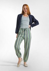 Niebieska lniana kurtka na jasnoniebieskim tank topie, zestawiona z zielonymi spodniami w paski z elastycznymi mankietami oraz kremowymi balerinami.