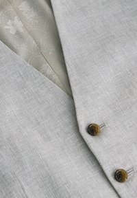 Blazer gris claro con dos botones marrones y forro interior con estampado floral visible en el cuello.