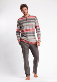 Camisa de manga larga a rayas en gris, rojo y verde con cuello tipo henley. Combinada con pantalones grises sólidos, la tela parece suave y ligera.