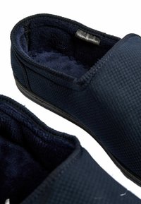 Mörkblåtofflor med en texturerad yta, mjukt innerskikt och en svart gummisula. En etikett märkt "THERMOWARMTH™" är synlig.