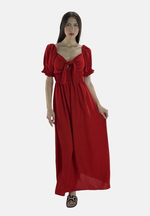 Robe maxi rouge avec des manches bouffantes, taille smockée et un nœud devant. Tissu doux, silhouette fluide et décolleté ouvert. Sandales noires.