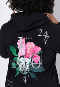 Zwarte hoodie met een kleurrijk grafisch ontwerp van een schedel, rozen en tekst. Het ontwerp bevat roze bloemen en zilveren accenten.