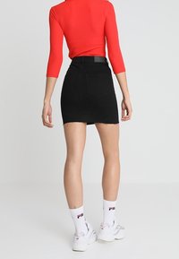 Falda mini de mezclilla negra con el dobladillo deshilachado, cintura alta y dos bolsillos traseros. Combinada con una blusa ajustada de manga larga roja y zapatillas blancas.