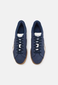Kék Reebok tornacipők fehér díszítésekkel és gumitalppal, felülnézetből, fehér háttér előtt.