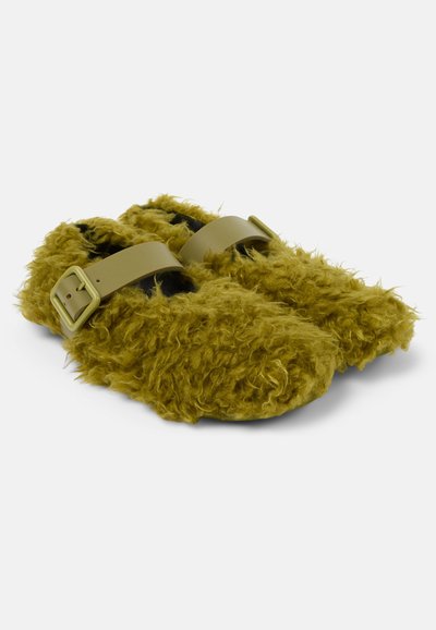 Furry olive green slippers with a textured surface. Features two thick beige adjustable straps with square buckles. Flat sole design.