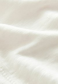 Material tricotat alb cu o textură moale și modele subtile, având o ușoară strălucire, prezentând pliuri netede și o cădere delicată.