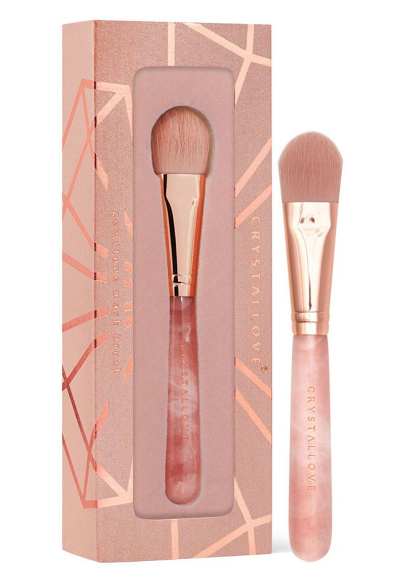 Pędzel do makijażu z różową rączką i miękkim włosiem, zapakowany w pudełko w geometryczny wzór w kolorze różowego złota z nazwą marki "CRYSTALLOVE."