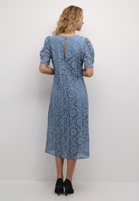 Lace dress in light blue with floral pattern, short puff sleeves, back keyhole cutout, and a midi length, paired with black high-heeled shoes.