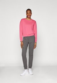 Svetter i lys rosa stoff, bred halslinje, lange ermer. Grå joggebukser, tapered fit, elastiske mansjetter. Hvite sneakers fullfører antrekket.