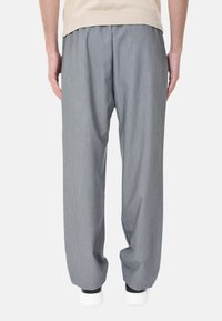 Pantaloni a gamba larga grigi realizzati in tessuto morbido, con una texture liscia e un design plissettato, abbinati a sneakers bianche.