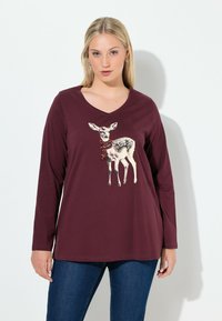 Burgundy pitkähihainen paita v-kaula-aukolla. Ominaisuuksina hirvi-kuva, joka on koristeltu punaisilla helmin. Pehmeää kangasta, rento malli. Esillä farkut.