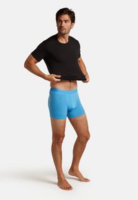 Svart bomulls t-shirt och blå modal boxershorts på en stående manlig modell, som visar en figursydd design med en slät yta.