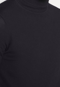 Schwarzer Rollkragenpullover aus einem glatten, dehnbaren Stoff. Verfügt über ein tailliertes Design mit gerippten Details am Kragen.