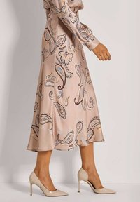 Ein langer, hellrosa Satinrock mit aufwendigen Paisleymustern in Blau, Braun und Orange, kombiniert mit beigen High Heels.