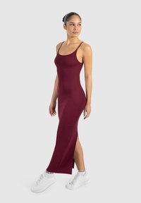 Vestido maxi burdeos con acanalado, tirantes finos y una abertura lateral, combinado con zapatillas blancas. Textura suave y diseño ajustado.