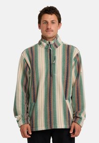 Fleece pullover, gestreept in groen, crèmekleur en roestkleur. Heeft een hoge kraag, een rits aan de voorkant en zijzakken. Zachte, textuurvolle stof.
