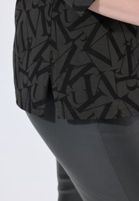 Top nero con motivo su fondo grigio scuro e lettering intricato; abbinato a pantaloni grigi eleganti, creando un look coordinato.