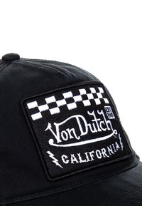 Black cap featuring a white embroidered patch with a checkerboard border and the text "Von Dutch EST 1981 CALIFORNIA." Smooth fabric texture.