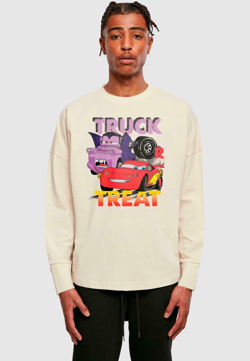 Gaiši bežs garo piedurkņu krekls ar multfilmu automašīnām un uzrakstu "TRUCK OR TREAT" boldā, daudzkrāsainā stilā. Gluda auduma faktūra.