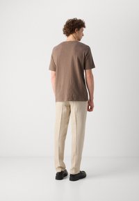 Brown short-sleeve shirt with a soft texture. Paired with light-colored, loose-fitting trousers and black shoes, shown from the back.
