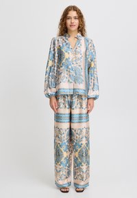Leichtes Satin-Pyjama-Set mit floralem und Paisleymuster in Blau und Gelb. Das Oberteil hat gepuffte Ärmel; die Hose ist weit und gemustert.