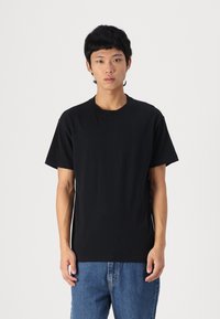 Black cotton t-shirt with a classic crew neck, short sleeves, and a straight cut. Worn with blue denim jeans.