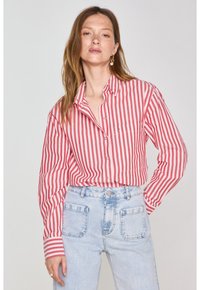 Camicia a righe rosse e bianche con maniche lunghe e una tasca sul petto, abbinata a jeans in denim azzurro chiaro a vita alta.