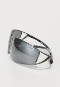 Lunettes de soleil avec des verres teintés gris, monture métallique gris, design semi-cerclé et branches bleu foncé avec logo.