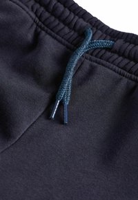 Marinblå sweatpants med en texturerad tyg, elastisk midja och ett flätat mörkblått snöre med plastspetsar.