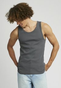 Débardeur gris à côtes avec un col rond, fabriqué à partir d'un matériau doux. Porté avec un short en denim bleu clair, montrant une silhouette ajustée.