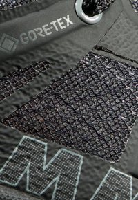 Schwarzer Wanderschuh aus strukturiertem Gore-Tex-Material, mit Mesh-Einsätzen und auffälligen Logodetails in kontrastierendem Stil.