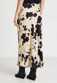 Jupe midi noire et beige en tissu fluide, ornée d'un motif éclaboussé. Associée à des bottines noires à motifs.