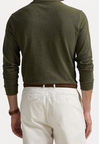 Forest green long-sleeve polo shirt with a collared neck, paired with cream-colored chinos; features a brown belt and buttoned back pockets.