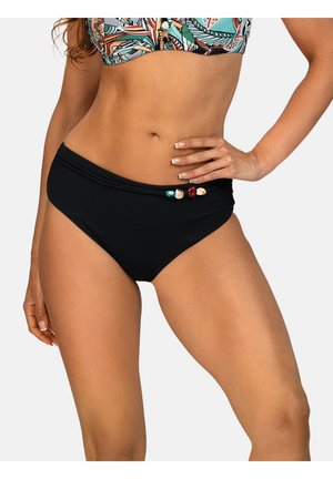 Kobieta ubrana w czarne bikini z koralikami i wzorzysty top bikini, pozująca z ręką na biodrze na jednolitym tle.