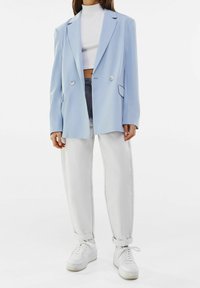 Light blue double-breasted blazer with notched lapels, paired with a white crop top, light grey jeans, and white sneakers. Smooth texture.