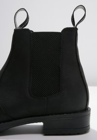 Black leather ankle boot with a textured elastic panel, loop pull tab, and low stacked heel. Smooth finish with a matte appearance.