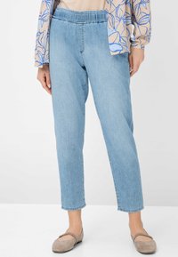 Pantalons en denim bleu clair avec une ceinture élastique, des jambes fuselées et une texture lisse. Associés à des chaussures plates beiges.