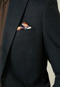 Donkerblauwe blazer met een gestructureerde weefsel, voorzien van een borstzak die een multikleurige zijden pochet van geometrische patronen bevat.